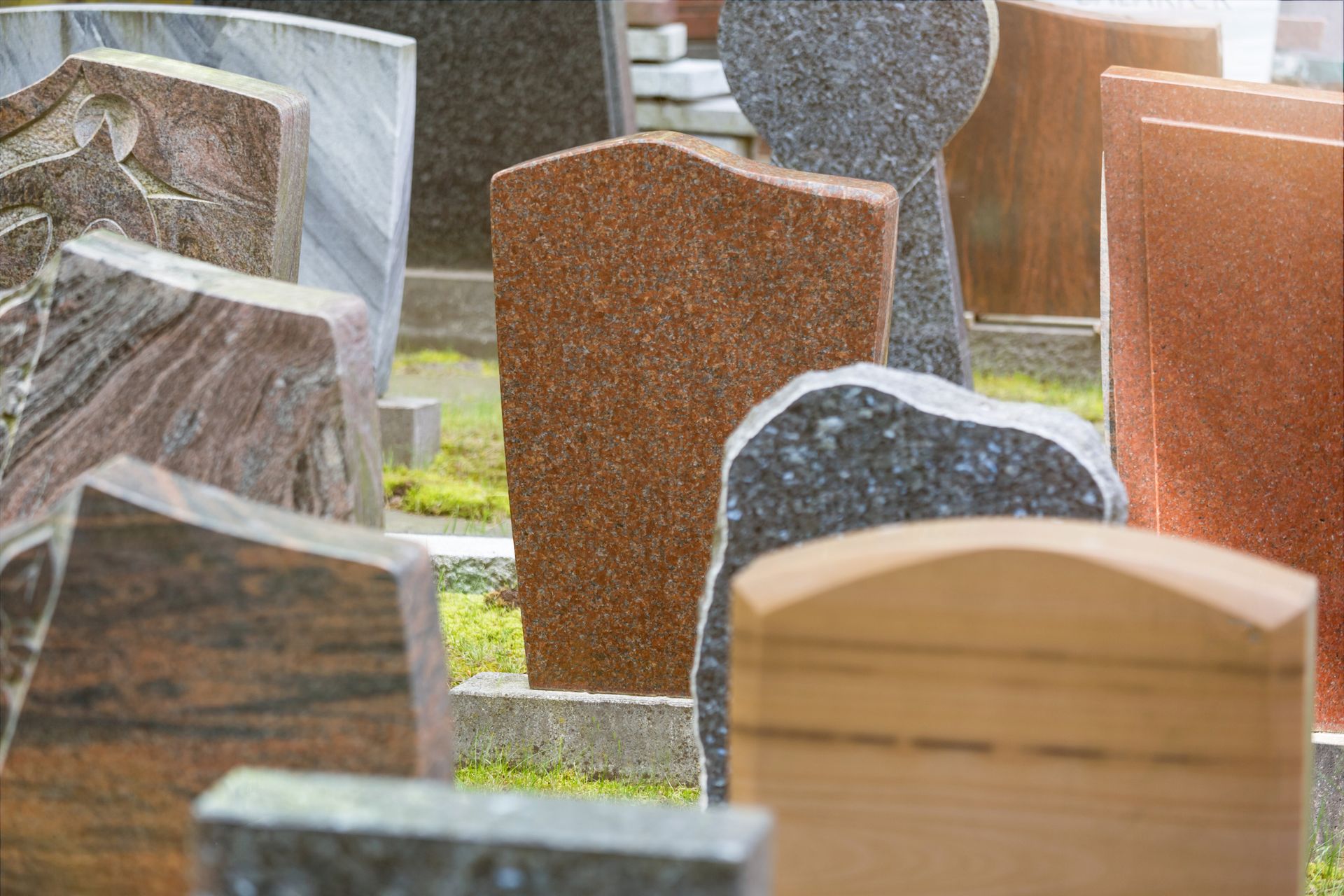 Heart-shaped memorial stone in a cemetery, a rose rests on top; sunlight highlights the scene.