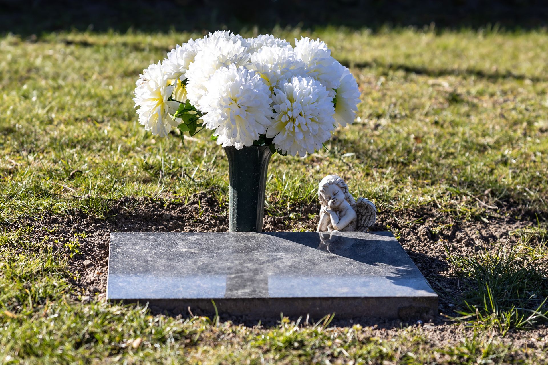 A blank gravestone on the meadow of a cemetery with white flowers.