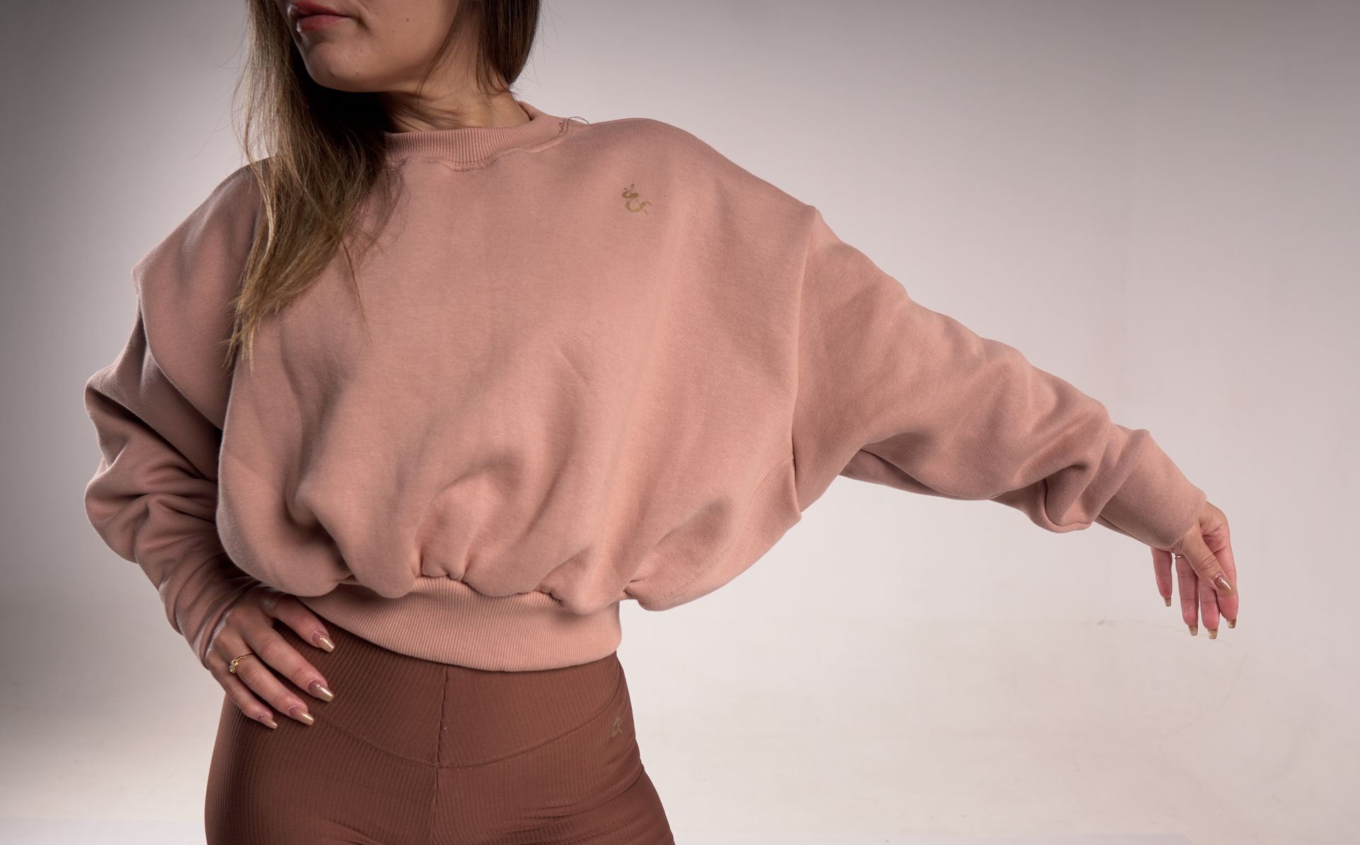 Mujer que viste una sudadera rosa y leggings marrones, extendiendo el brazo.