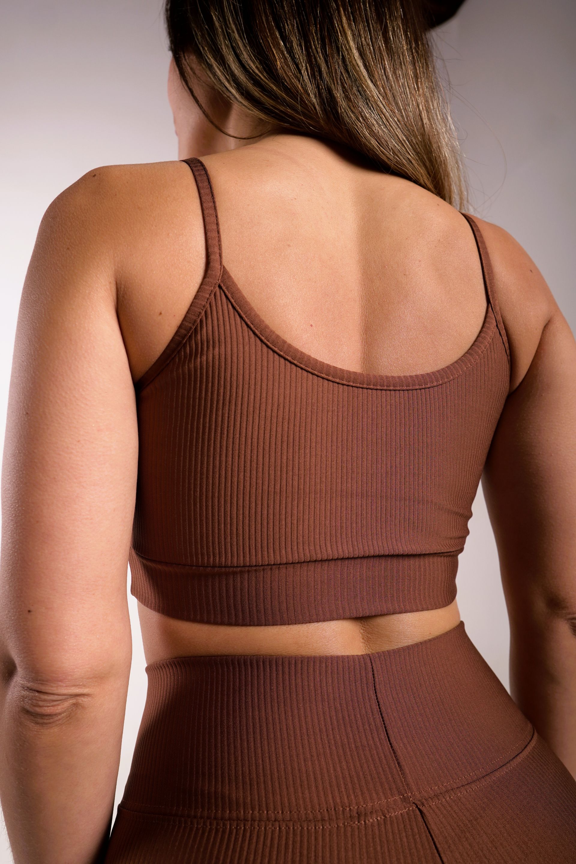 Mujer que lleva sujetador deportivo y leggings de canalé marrón, vista posterior.