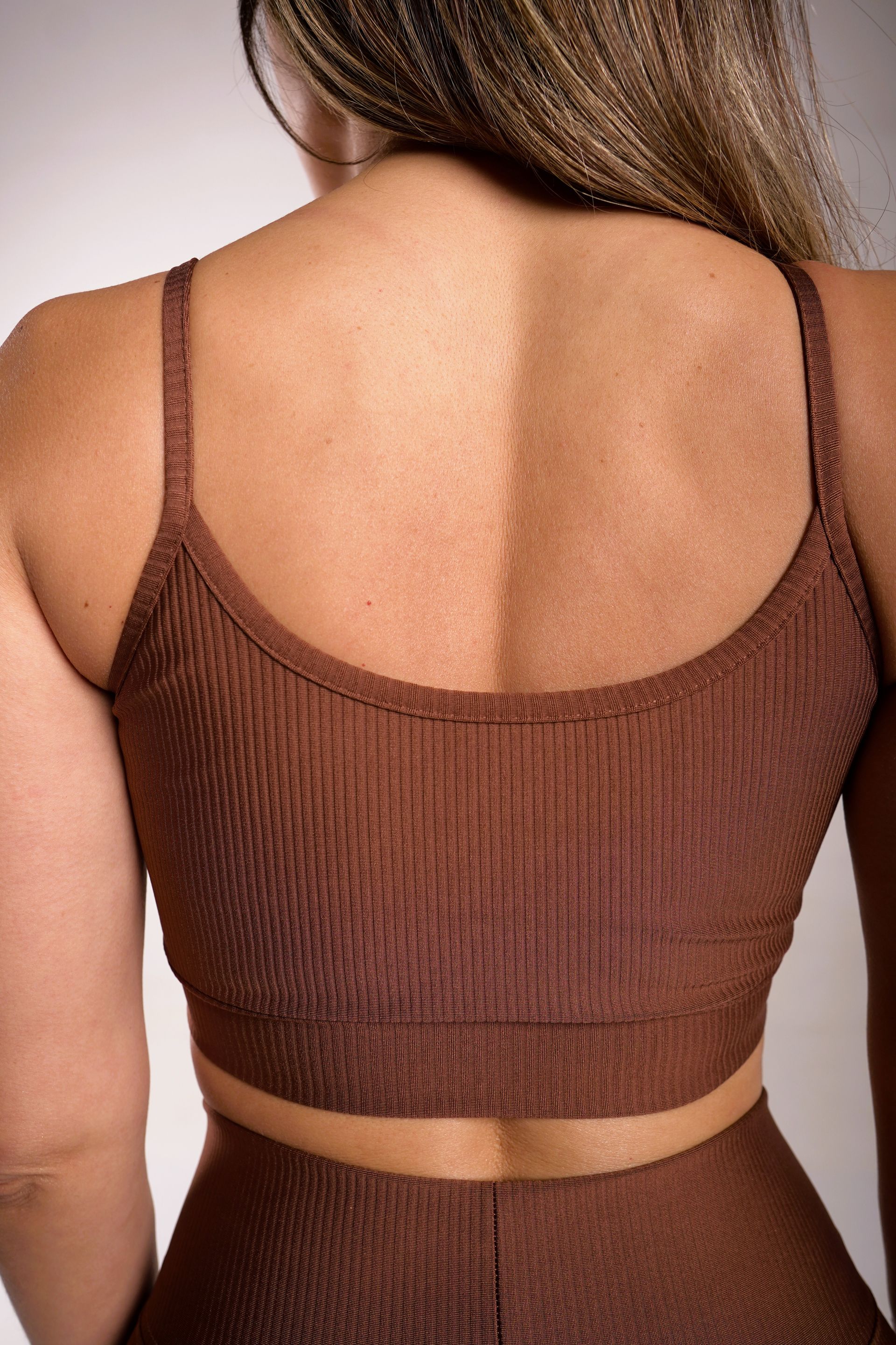 Mujer que lleva sujetador deportivo y leggings de canalé marrón, vista posterior.