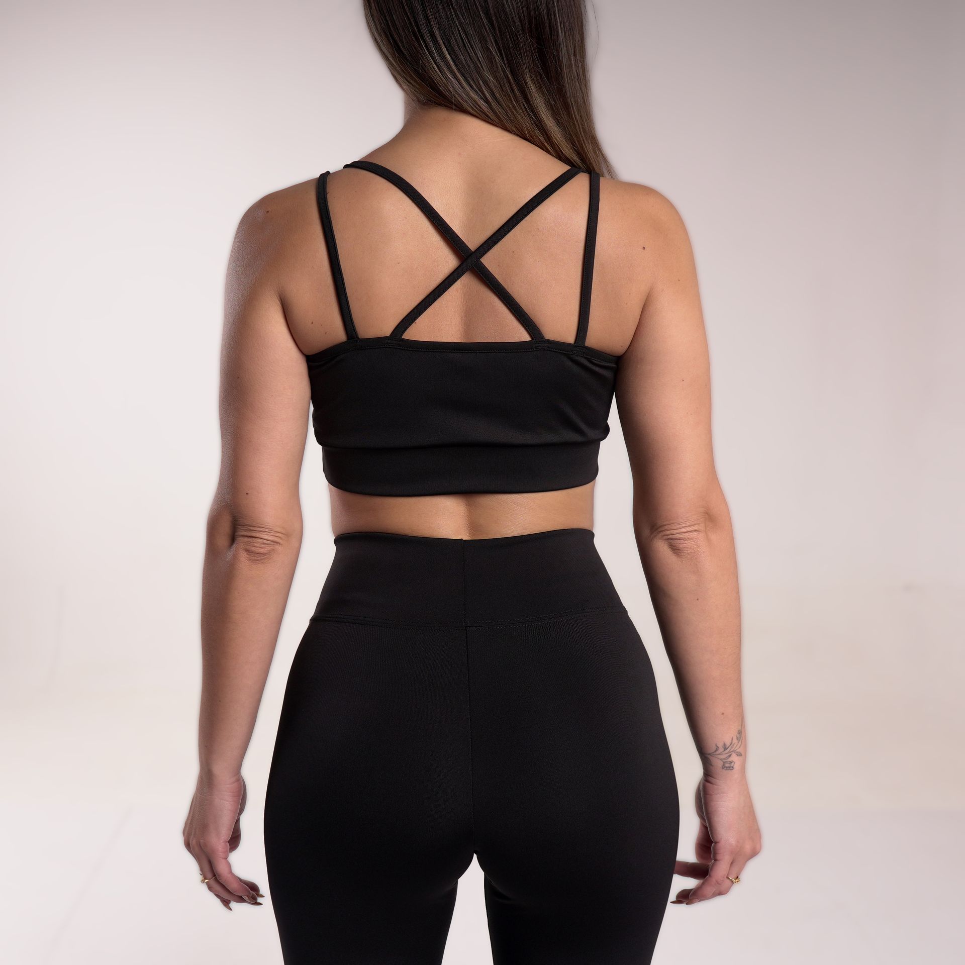Mujer de espaldas con sujetador deportivo negro con tirantes cruzados y leggings a juego.