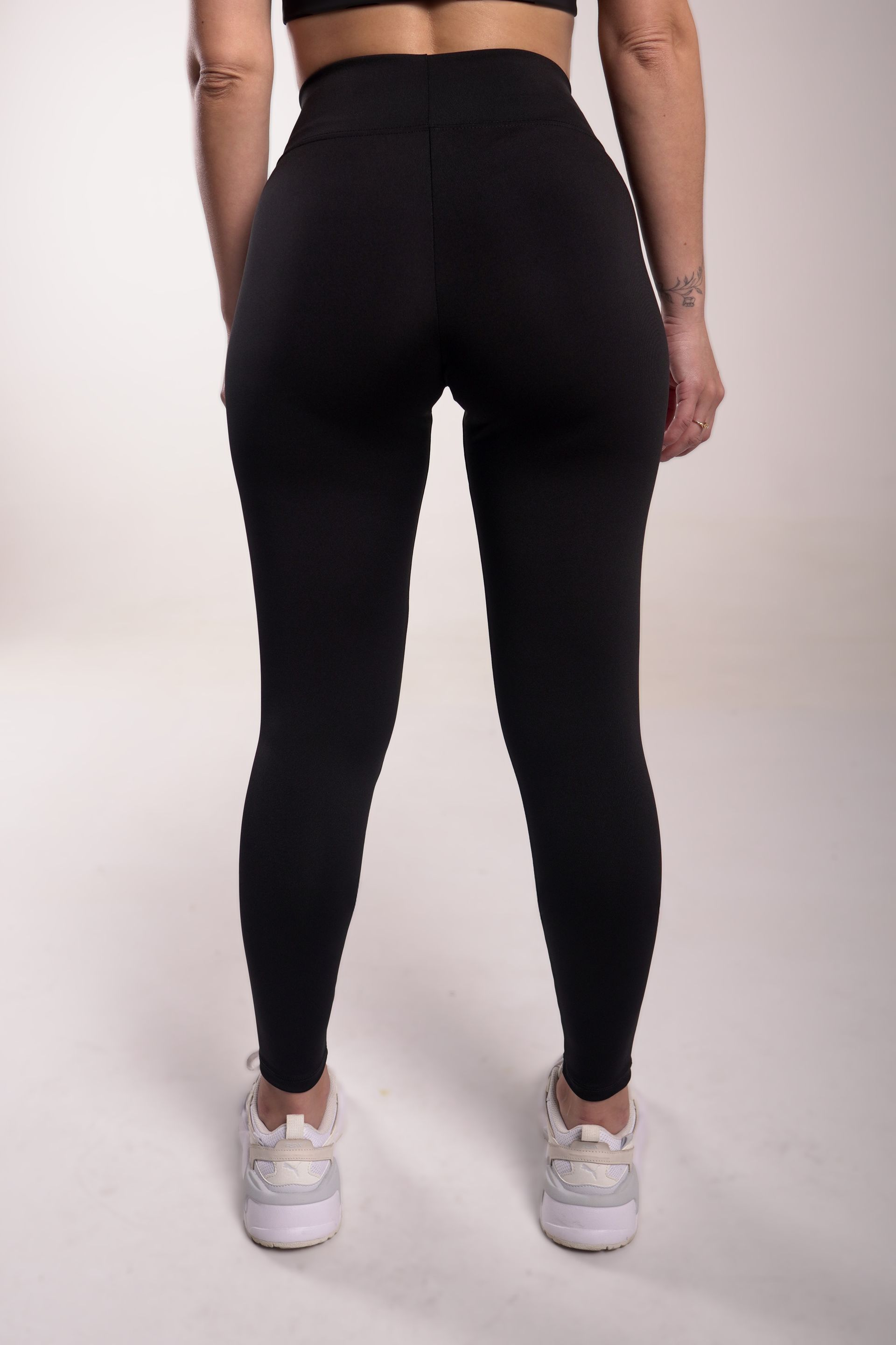 Mujer que viste leggings negros y zapatillas blancas, de pie sobre un fondo blanco.