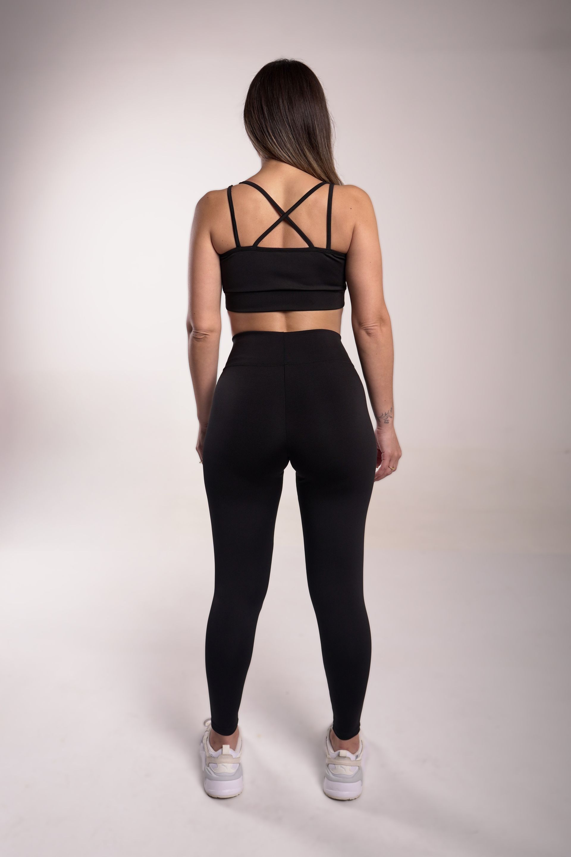 Mujer que viste leggings negros y zapatillas blancas, de pie sobre un fondo blanco.