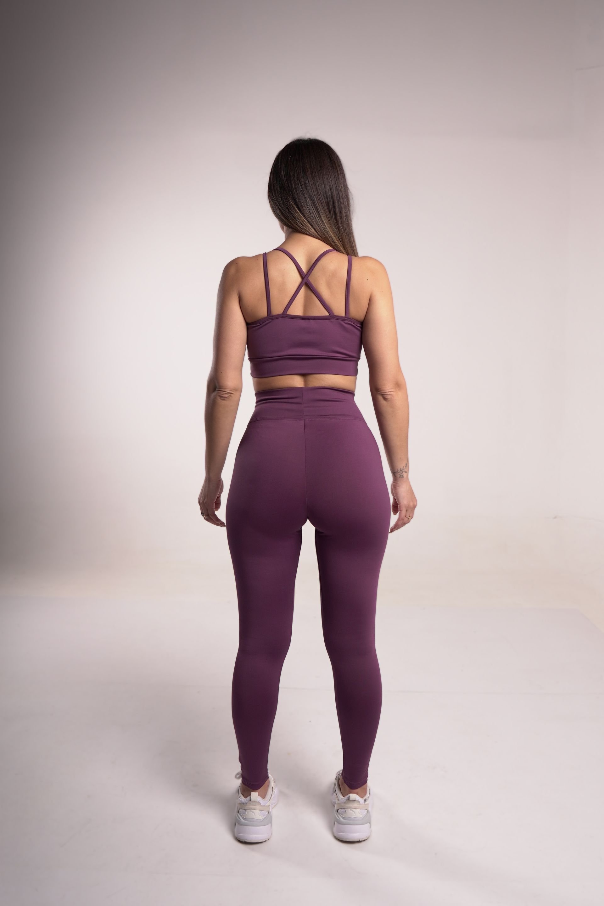 Mujer con un conjunto deportivo morado, de pie de espaldas a la cámara, en un estudio.