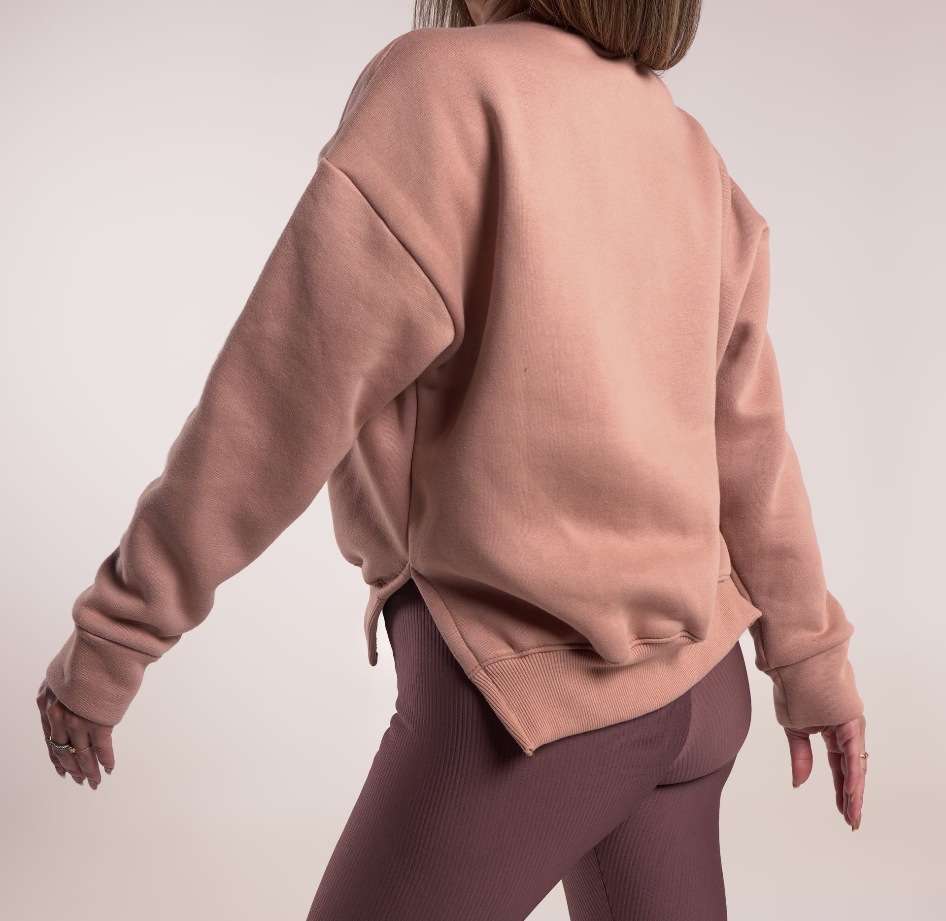 Mujer con sudadera rosa y leggings; vista posterior.