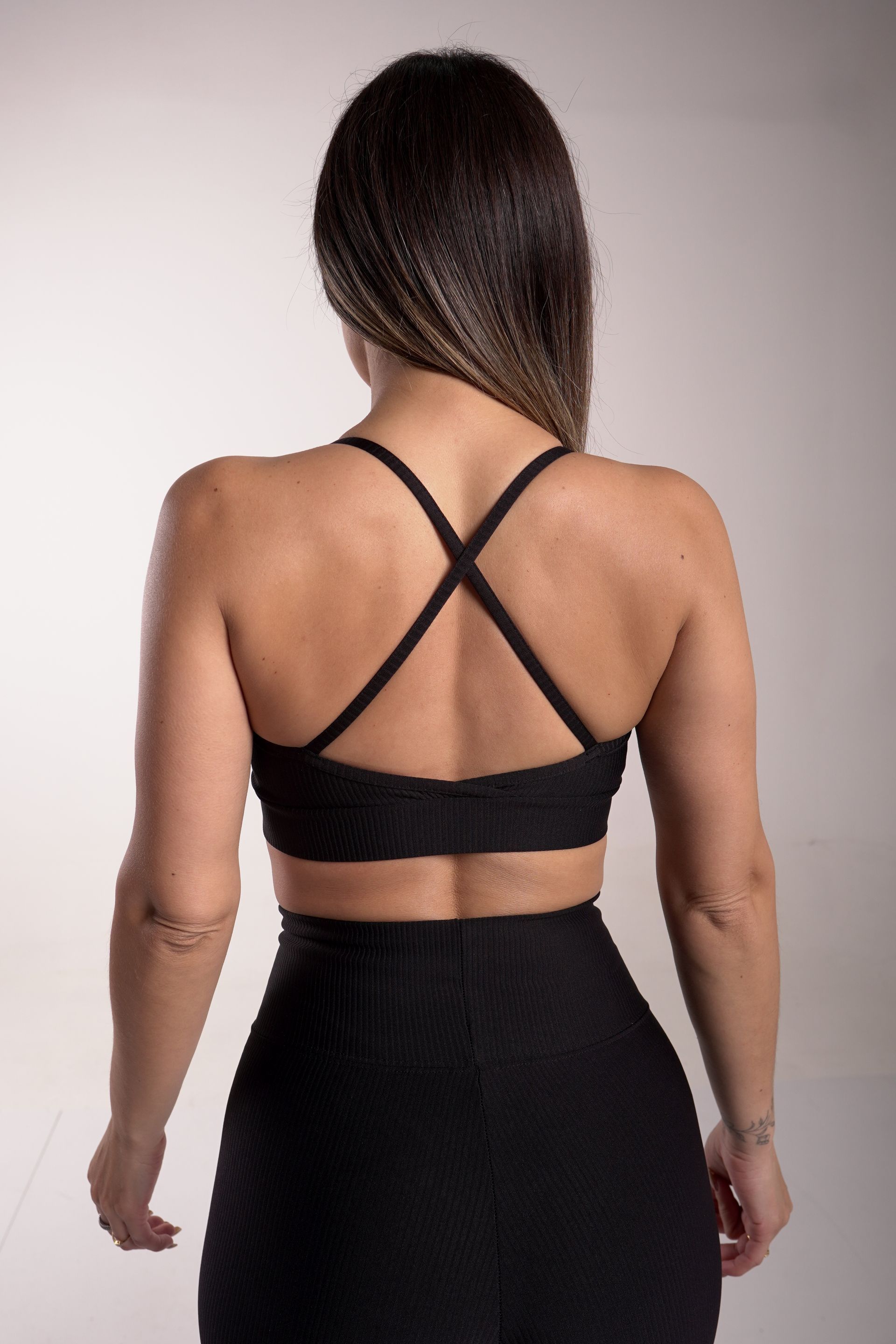 Mujer vestida con ropa deportiva negra, vista posterior, sobre un fondo blanco.