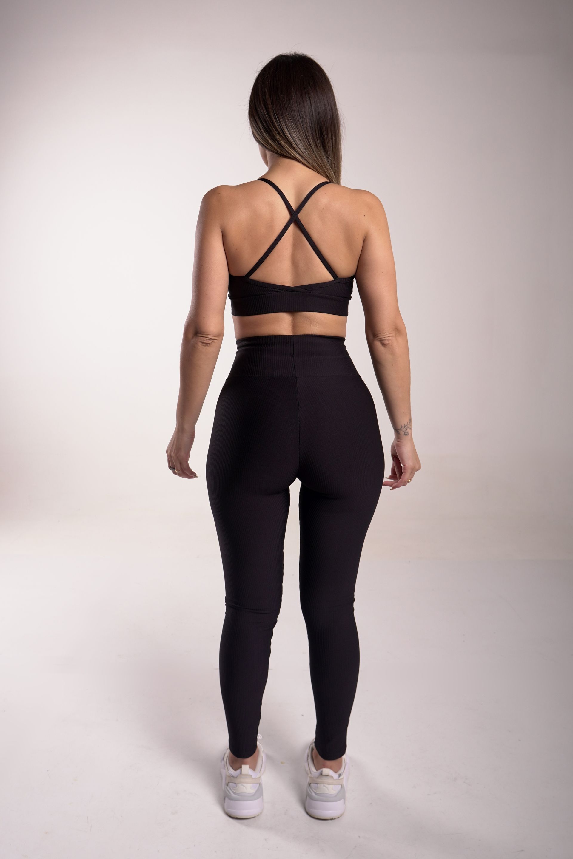 Mujer vestida con ropa deportiva negra, de espaldas, en un estudio.