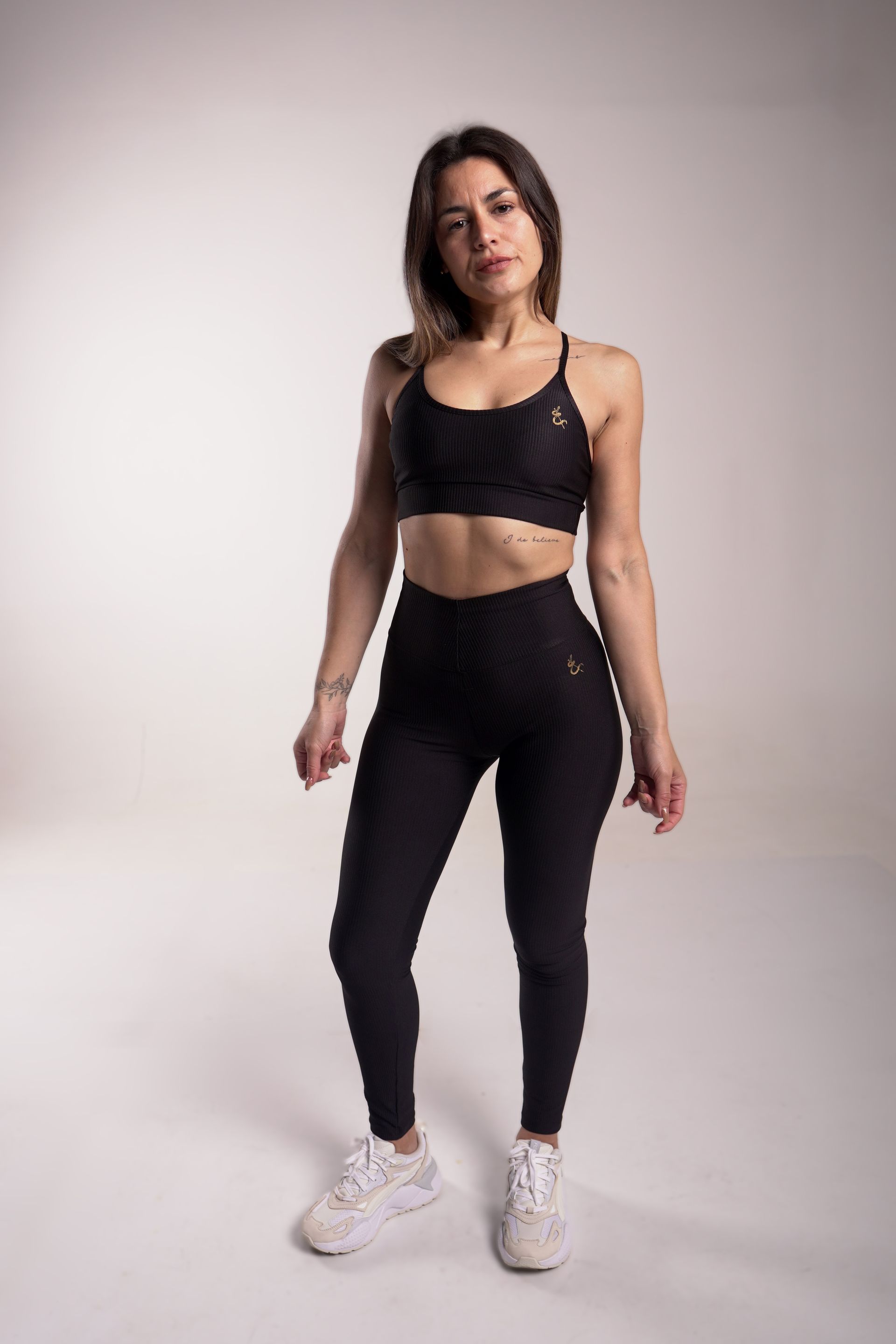 Mujer vestida con ropa deportiva negra, de espaldas, en un estudio.
