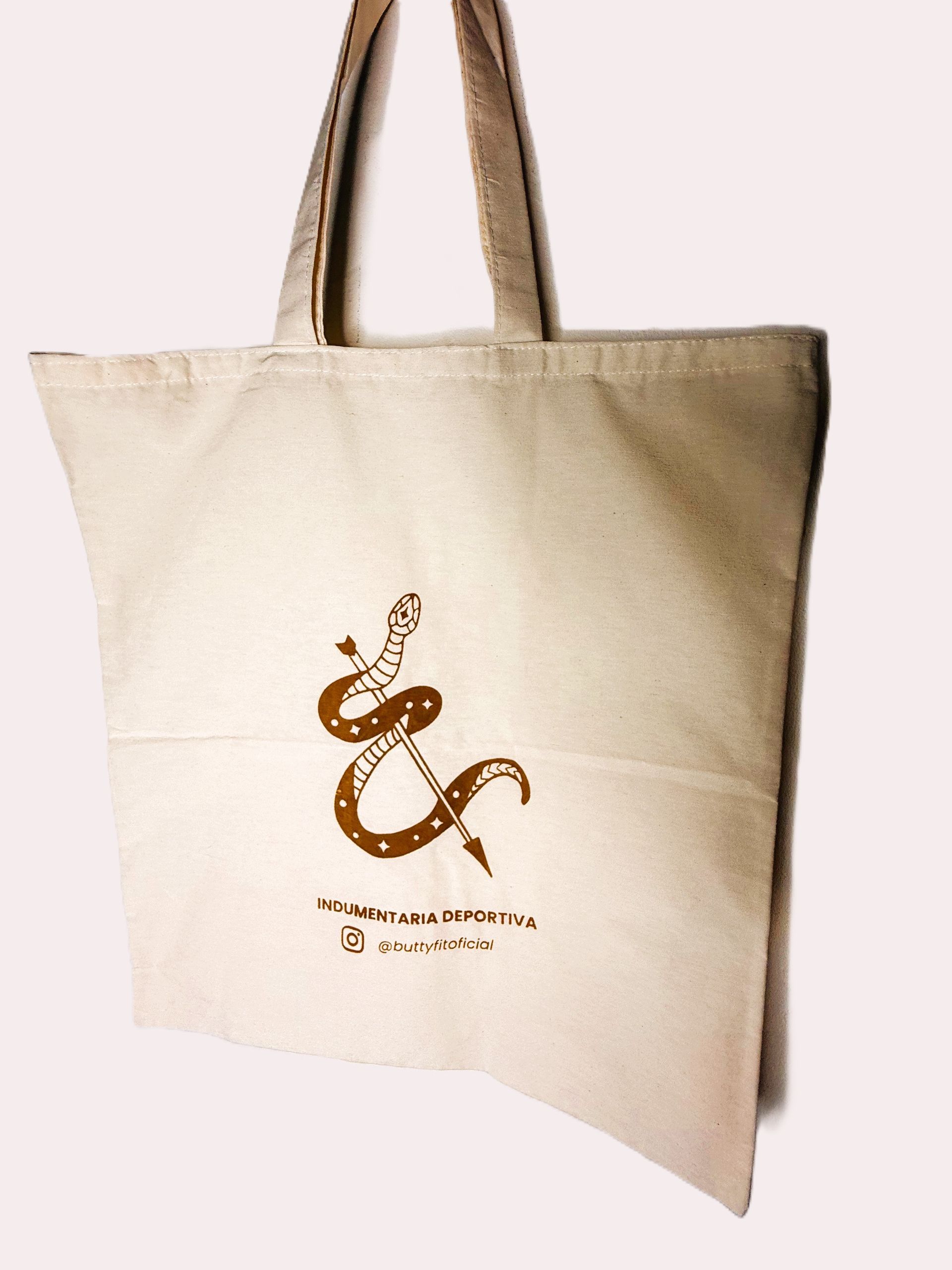 Bolso de mano beige con diseño de serpiente marrón y texto, "El símbolo de la serpiente 100% algodón".