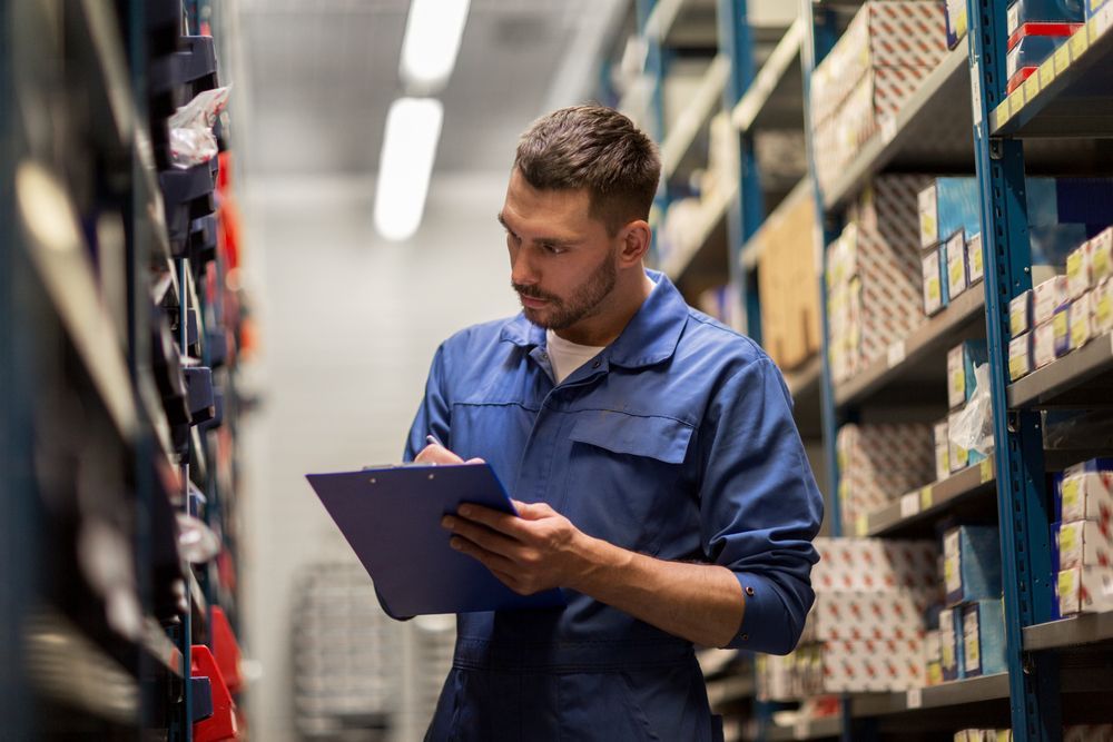 A man is looking at a clipboard in a warehouse.