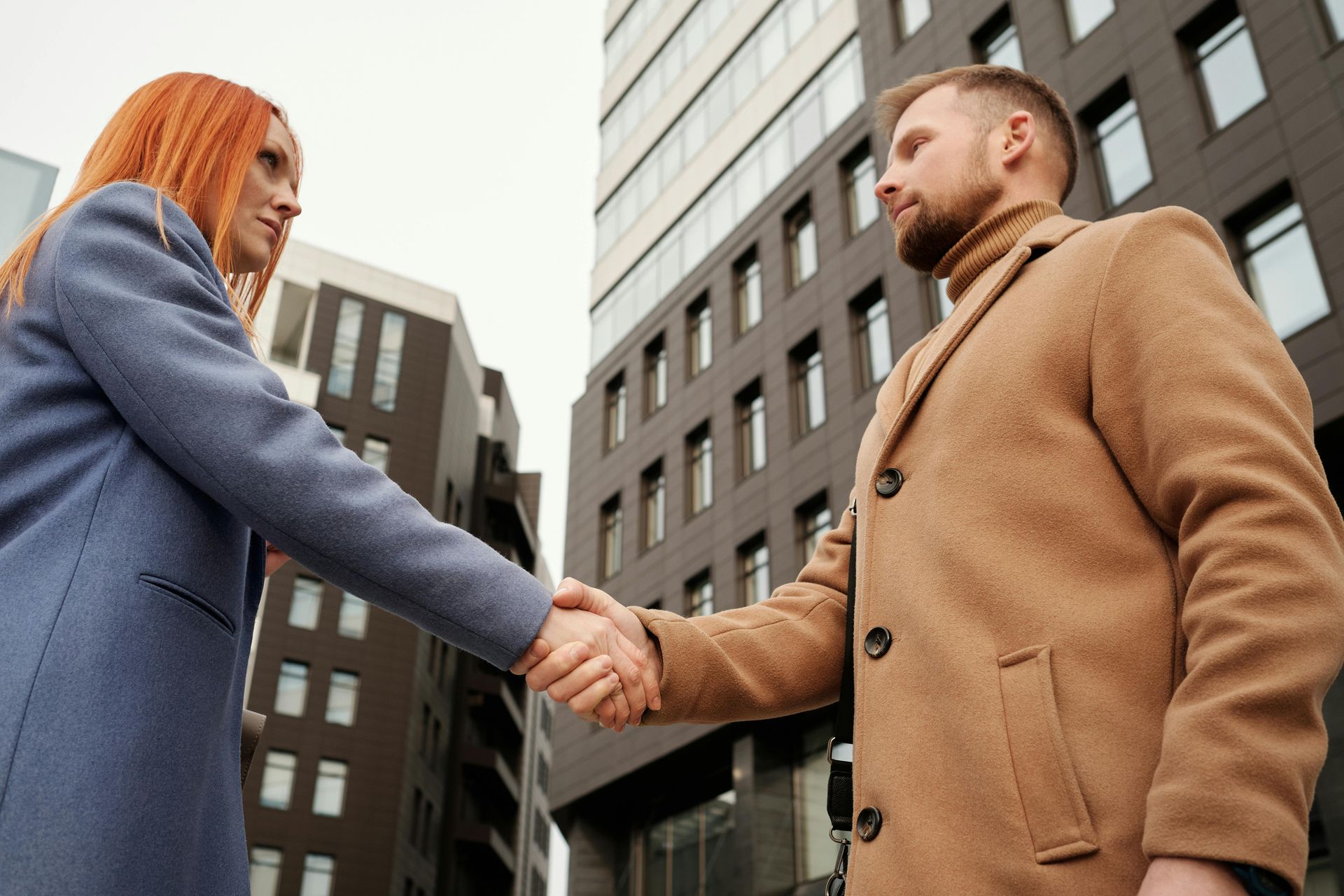 Two people shaking hands outdoors near office buildings.