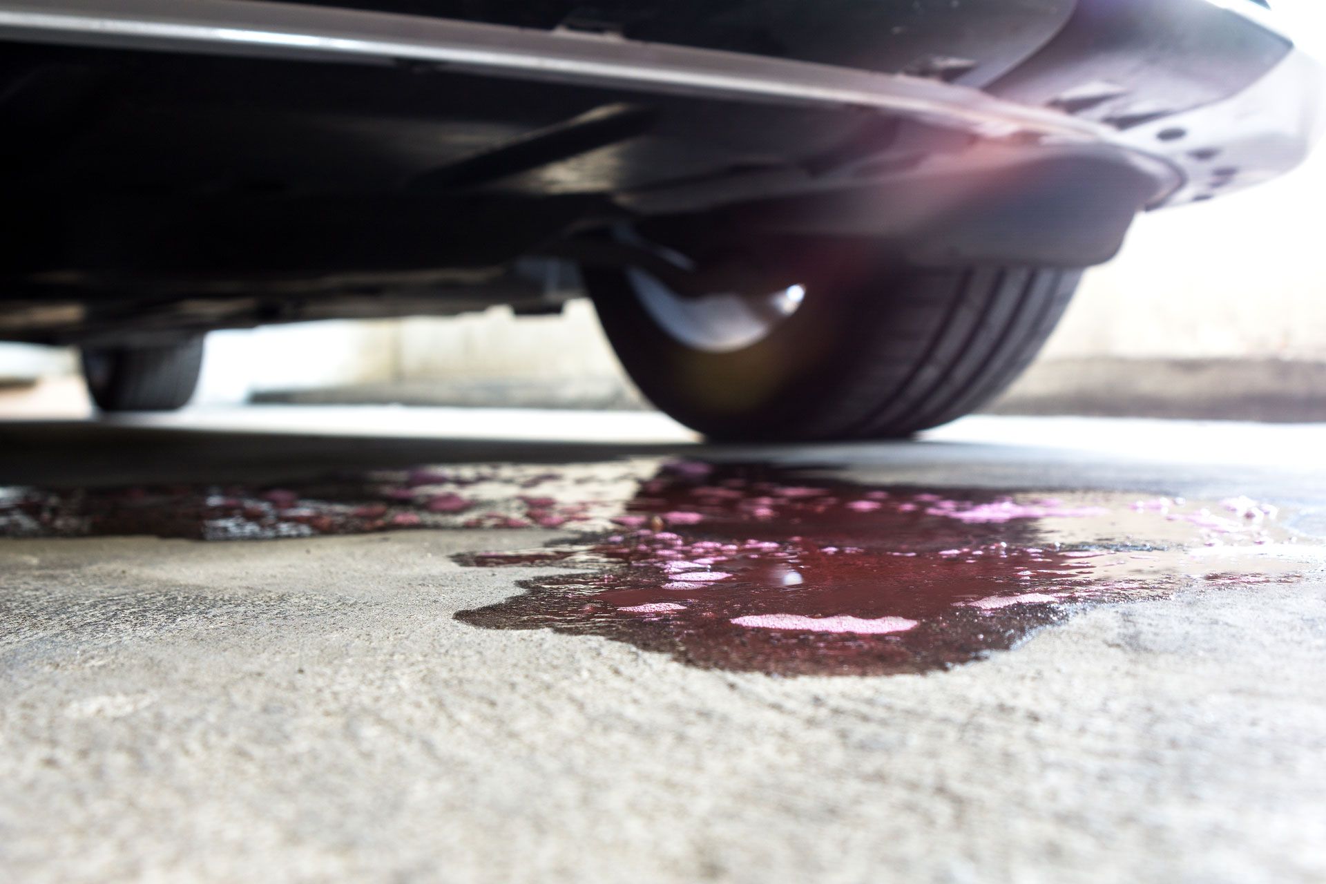 Car leaking pink fluid onto concrete.