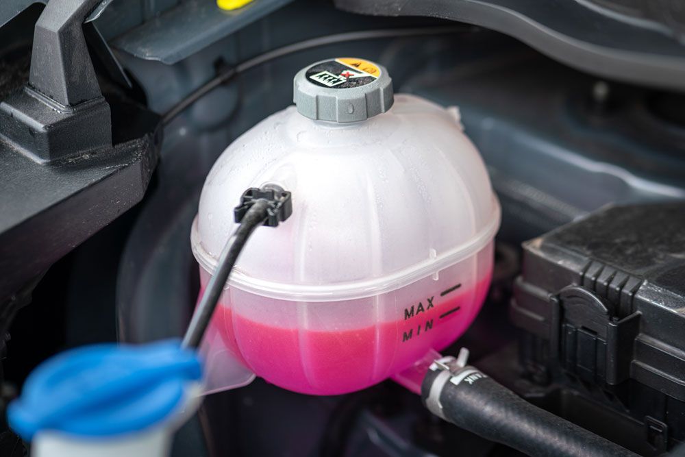 Coolant reservoir in car engine bay; pink coolant at MIN level.