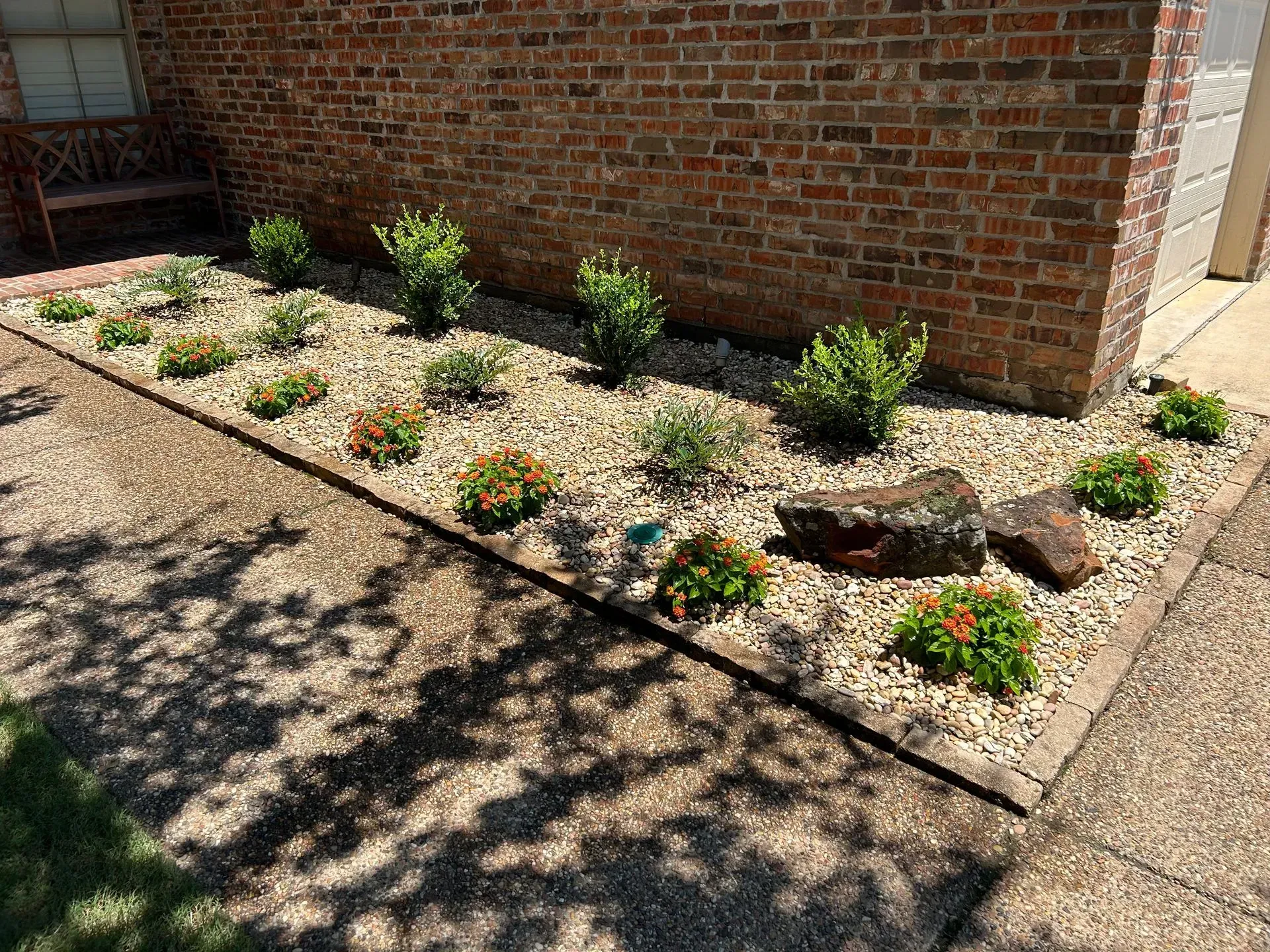 Xeriscaped flower bed with small shrubs and colorful ground cover along a brick wall.
