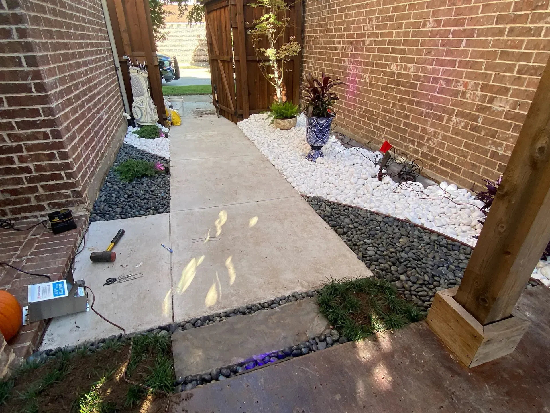 Narrow brick-sided walkway with concrete path, white gravel beds, and small garden decorations