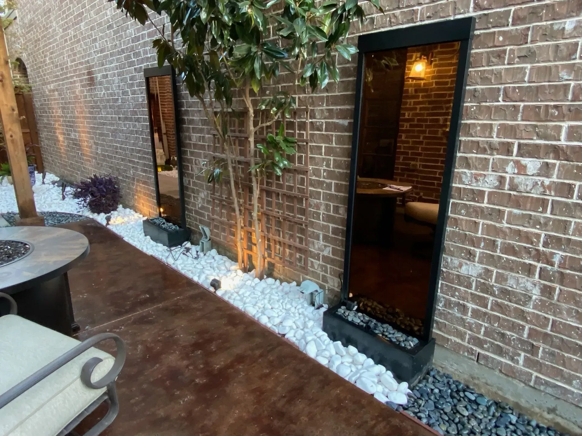Brick patio with a lit doorway, table, and white decorative stones along the wall.