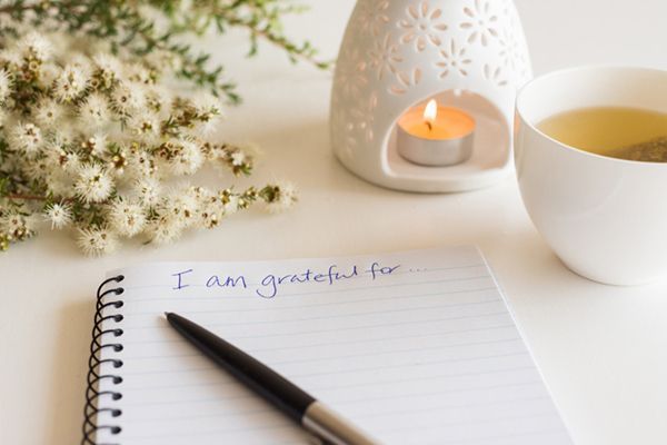 a notebook with the words `` i am grateful for '' written on it next to a pen and a cup of tea .