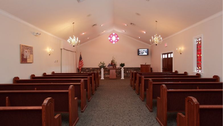 A church with rows of wooden benches and a stained glass window.