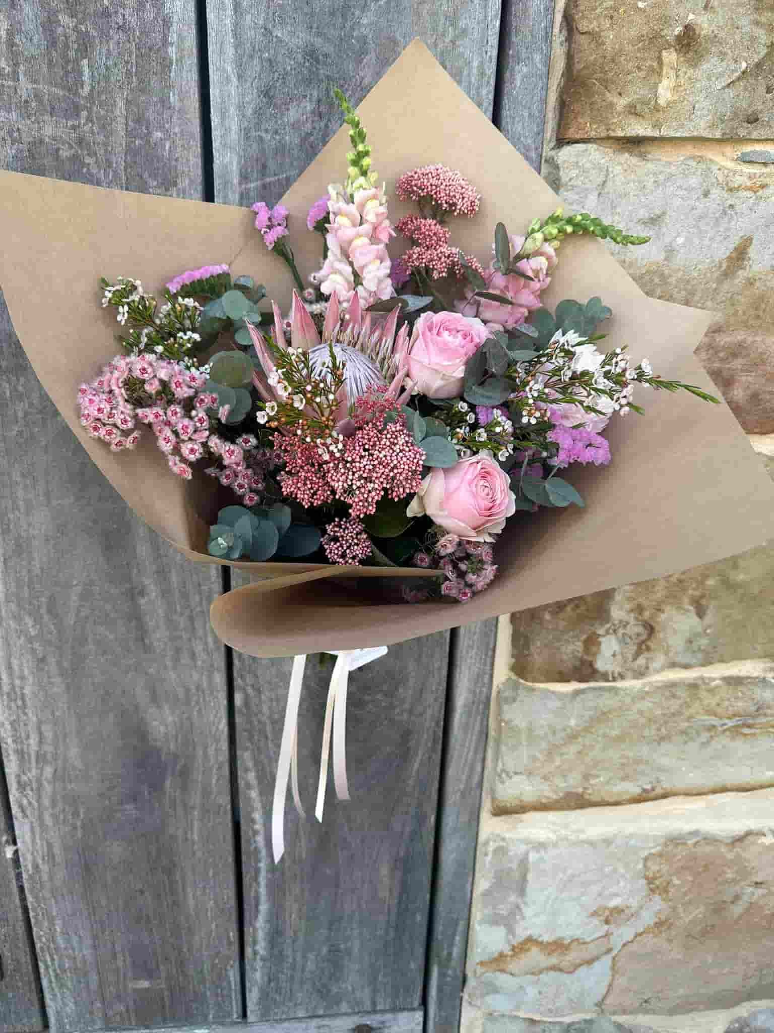 a Bouquet of Pink Flowers Wrapped in Brown Paper is Sitting on a Wooden Table — Flowers by Suzanne in Morpeth, NSW