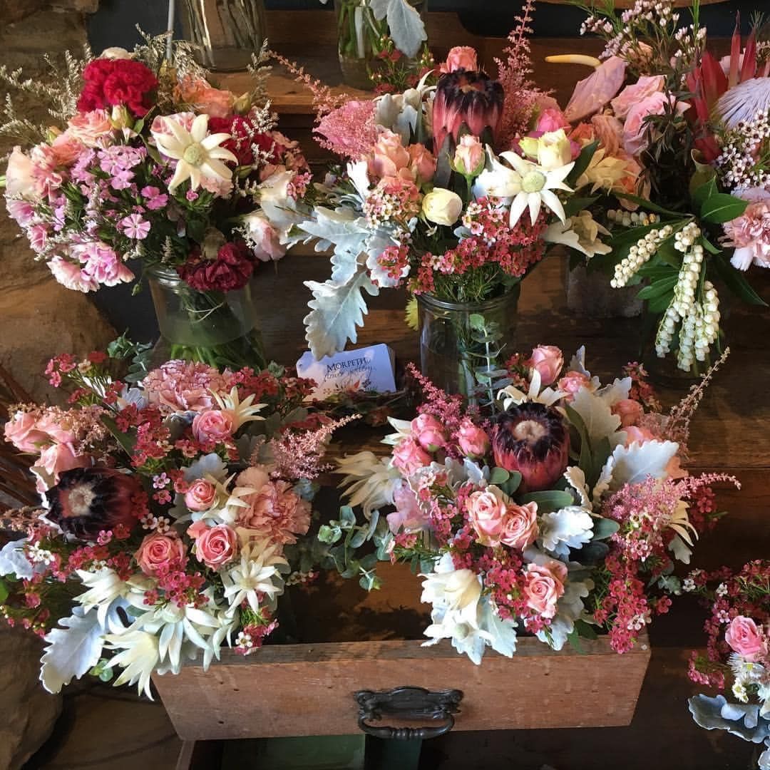 Several bouquets of pink and red flowers in a wooden drawer and mason jars on a table.