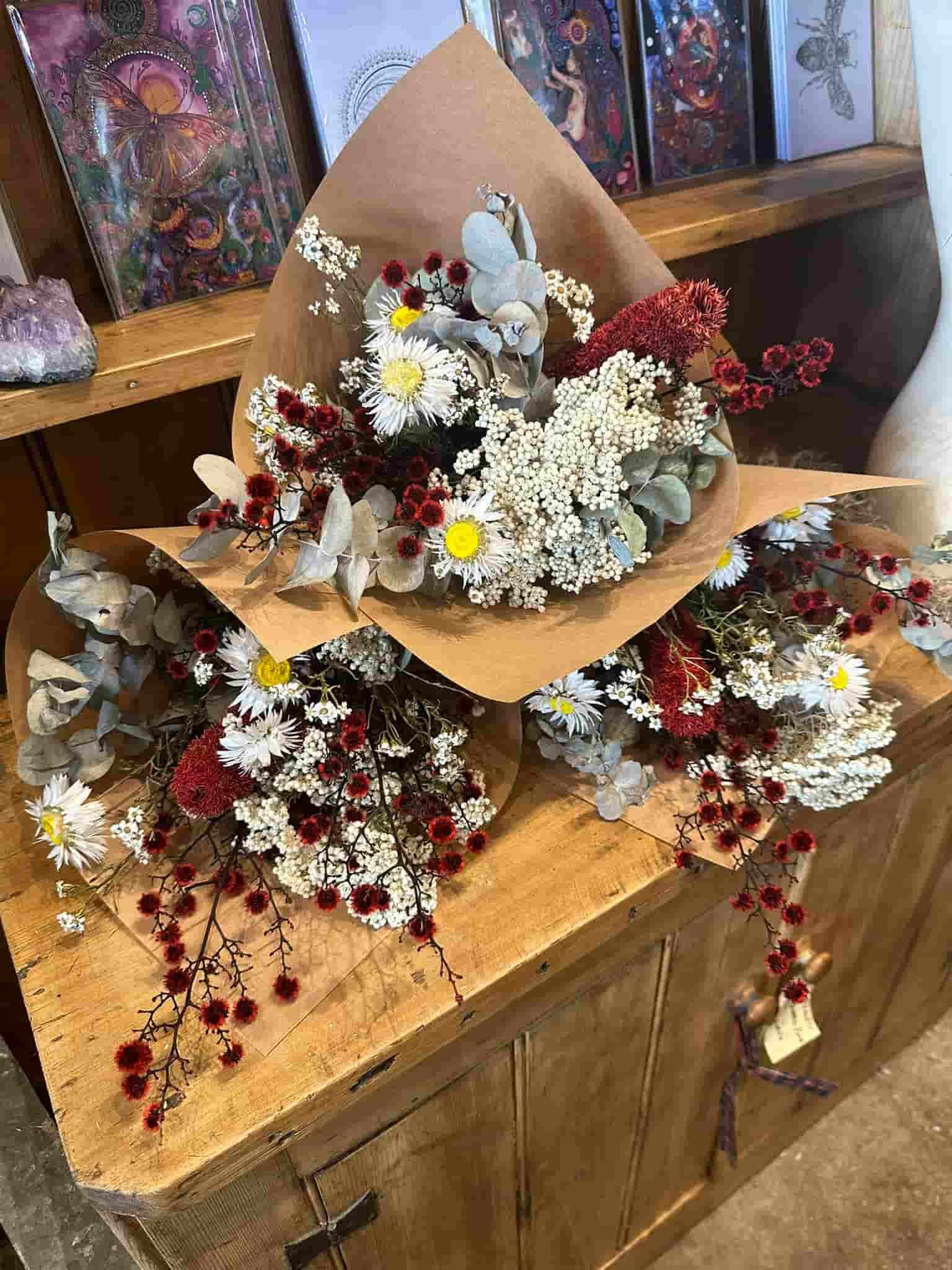 Three bouquets of dried flowers wrapped in brown paper on a wooden surface.
