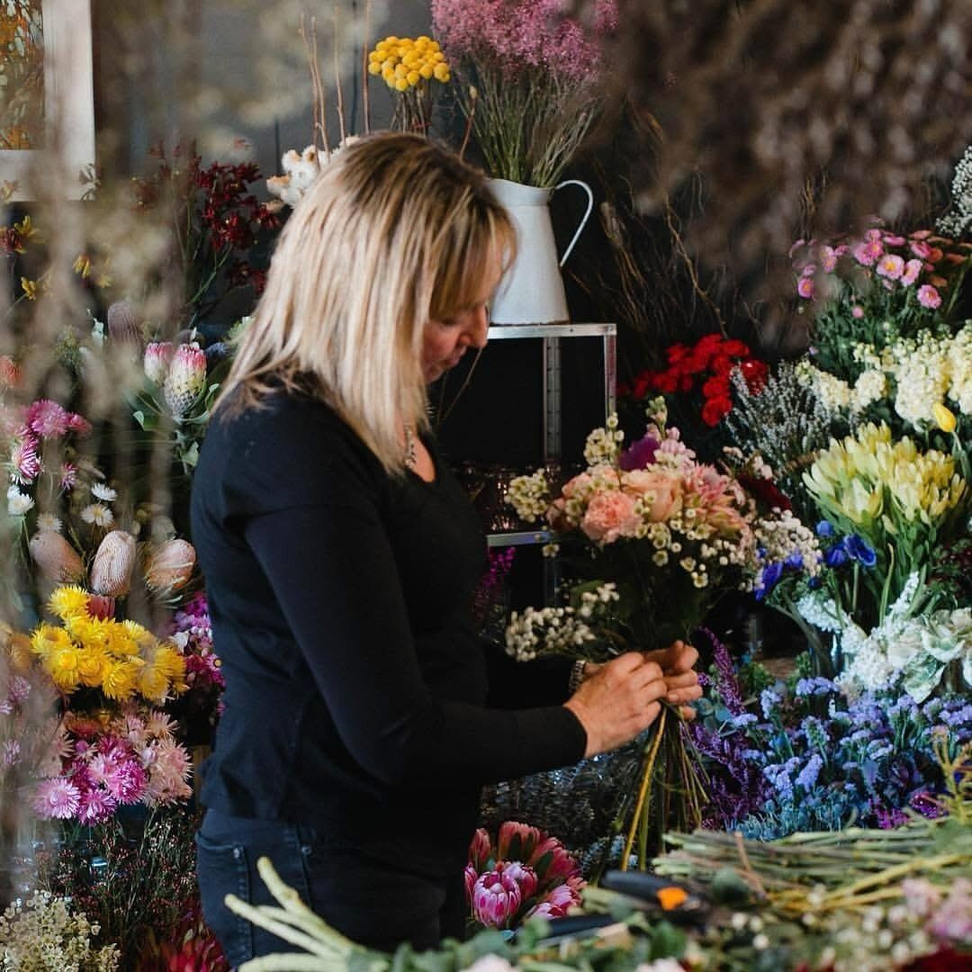 Woman arranging flowers in a shop, surrounded by colorful blooms.