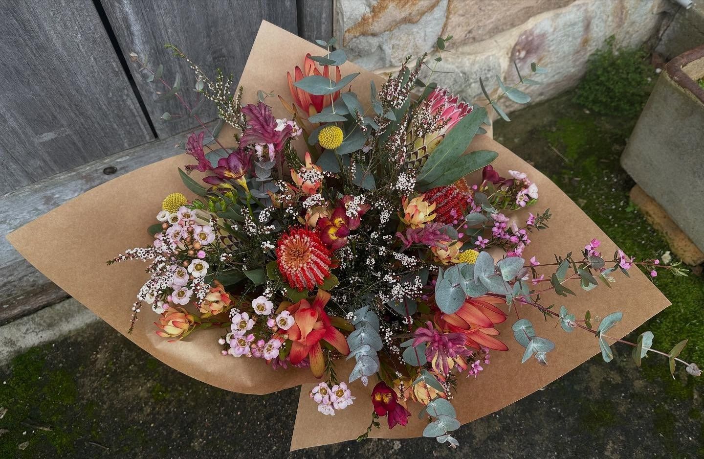 Bouquet of colorful flowers wrapped in brown paper, outdoors.