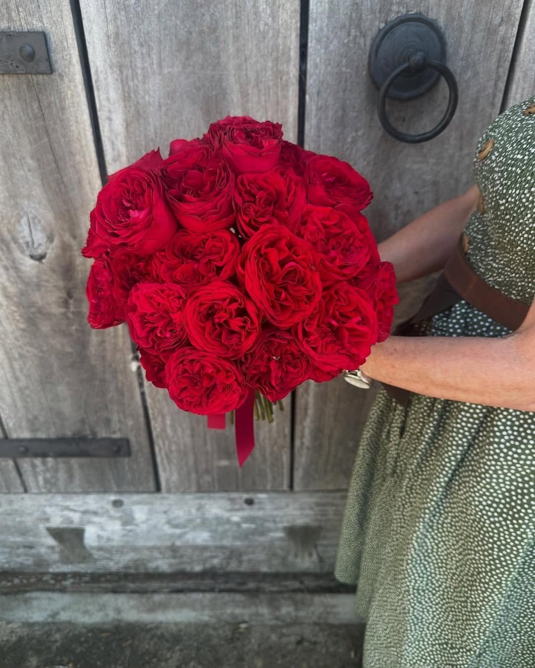 Woman holding a lush bouquet of red roses against a weathered wooden door.