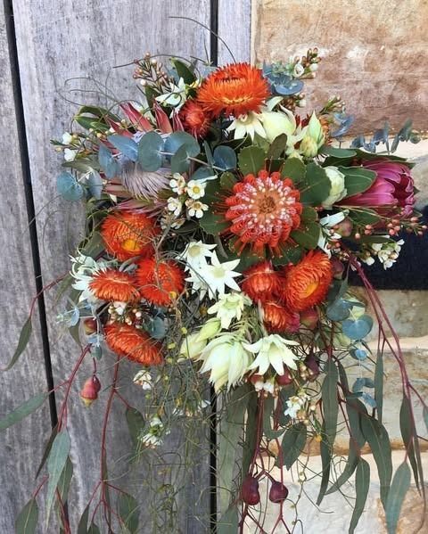 Bouquet of vibrant orange and white flowers with green leaves, against a wooden background.