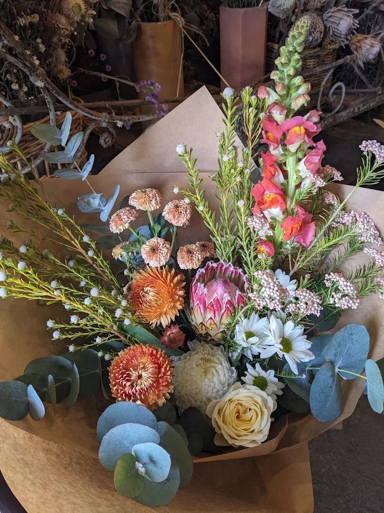 Bouquet of dried flowers in various colors, wrapped in brown paper, on a wooden surface.