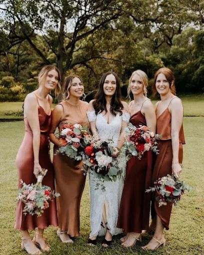 Bride with bridesmaids in rust-colored dresses holding bouquets outdoors.