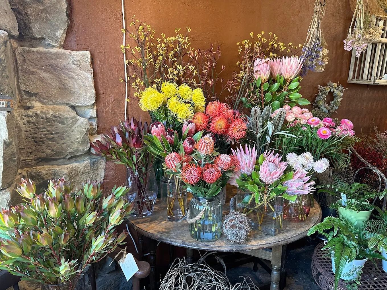 Flowers in vases on a rustic table in a shop, featuring various colors: pink, yellow, orange, and green.