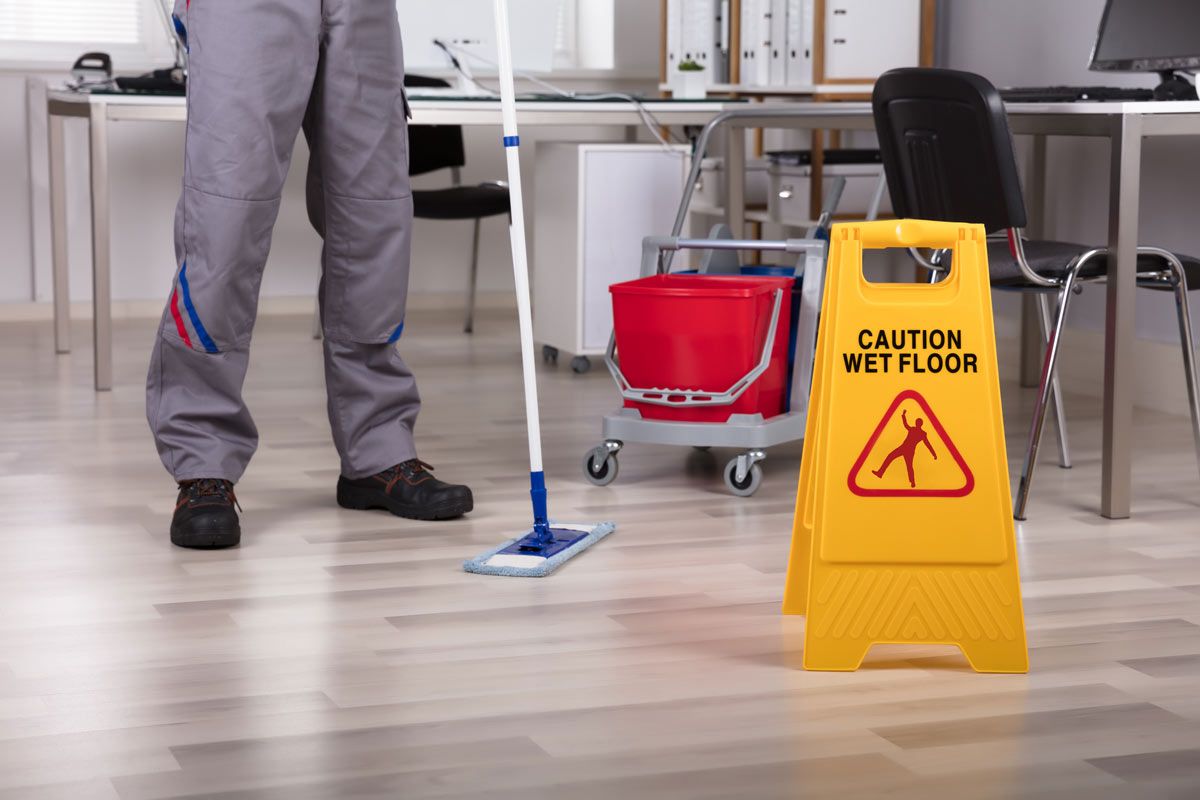 A man is mopping the floor in an office next to a caution wet floor sign