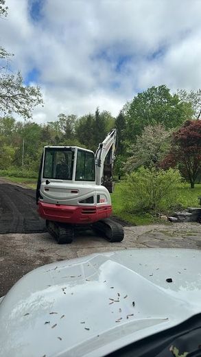 White and red excavator parked on dirt, trees in background. Overcast sky.