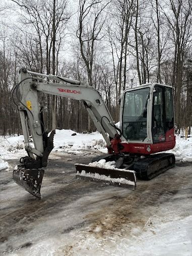A red and gray excavator parked on a snow-covered road in a forest.