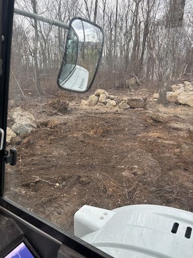 View from a machine cab clearing brush; dirt and rocks surround.
