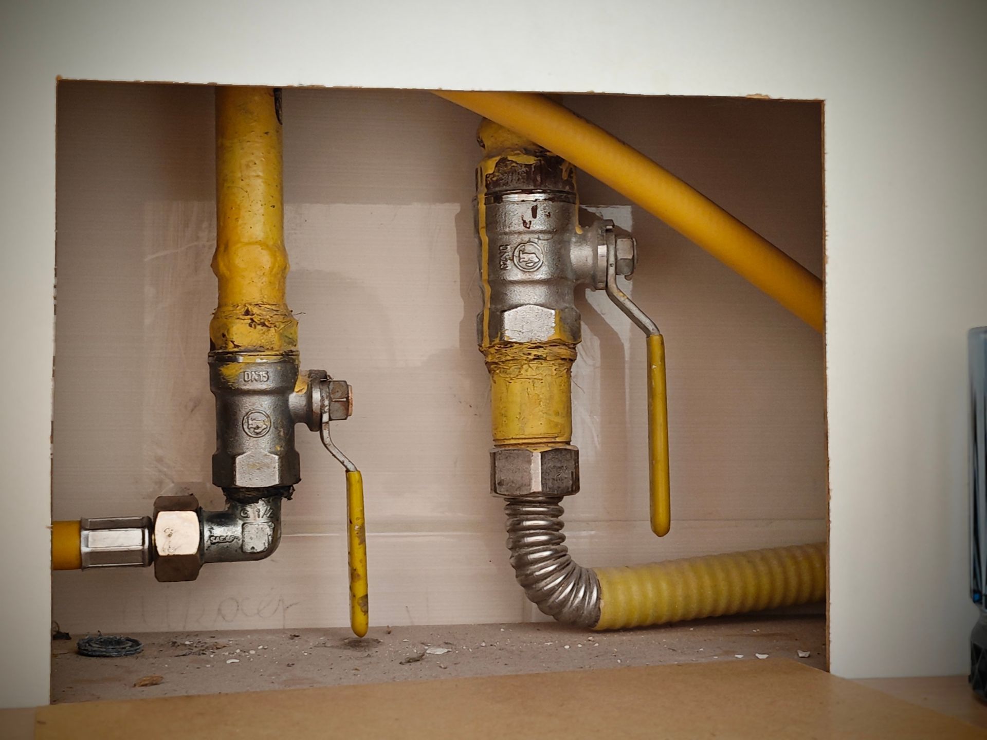 Two exposed gas pipes with yellow shutoff valves inside a wall opening