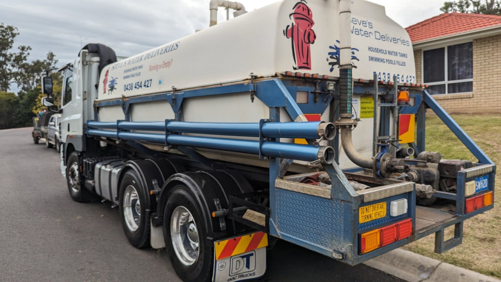 A white water tanker truck parked on a residential street with a prominent red fire hydrant graphic on the tank.