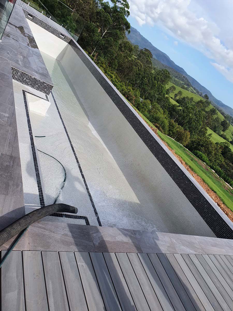 An empty infinity pool overlooks a lush, hilly green landscape under a bright, partly cloudy sky.