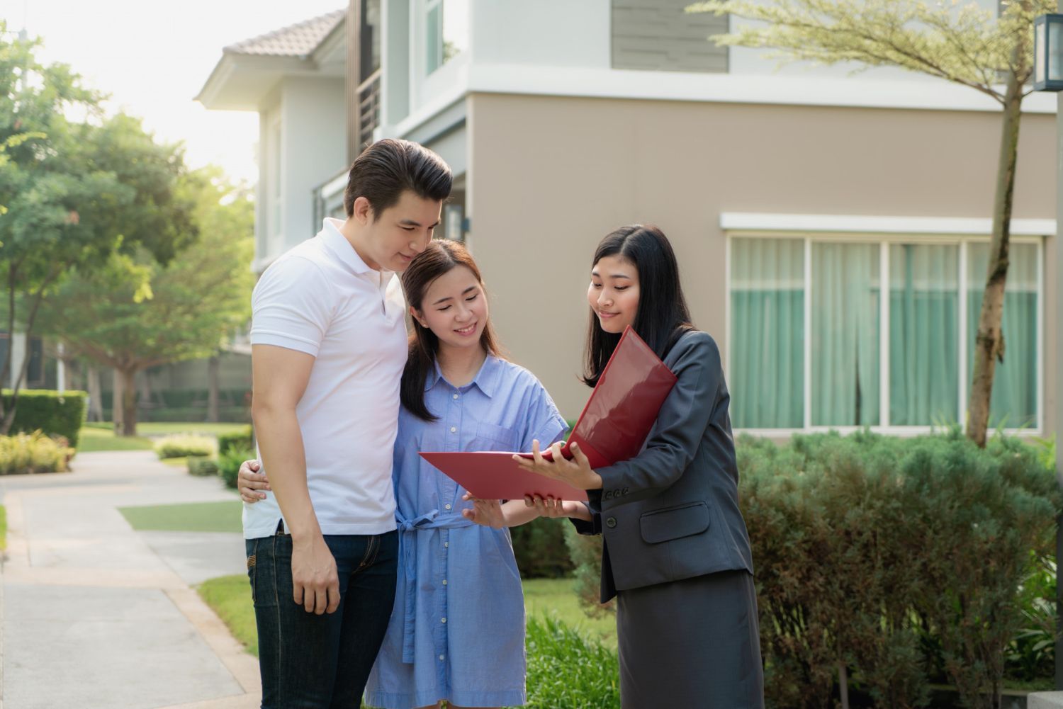 Couple looking at paperwork with a real estate agent in front of a house.