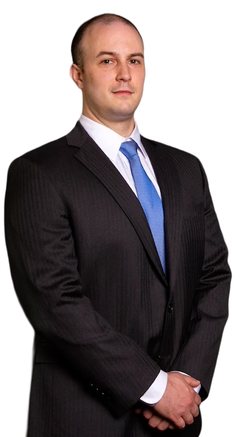 Patrick Welch in dark suit, blue tie, arms crossed, standing with smile.