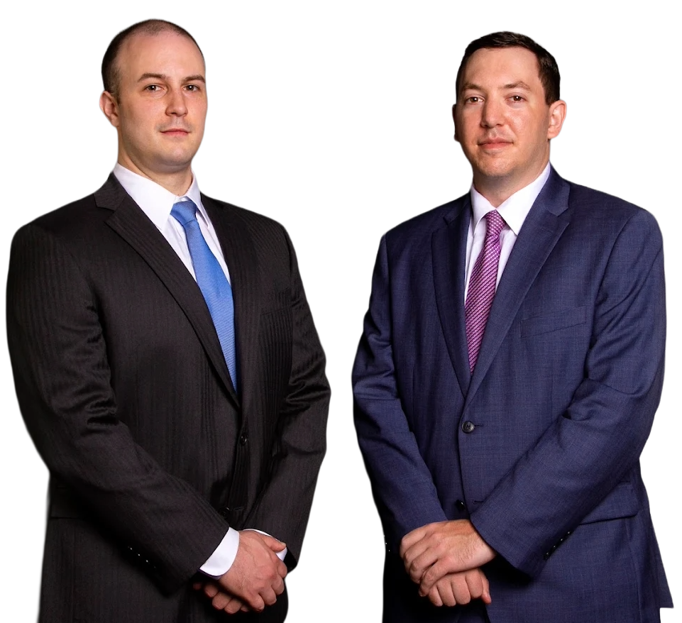 Patrick and Steven in suits, standing side-by-side, each with folded hands. One wears a blue tie, the other a purple tie.
