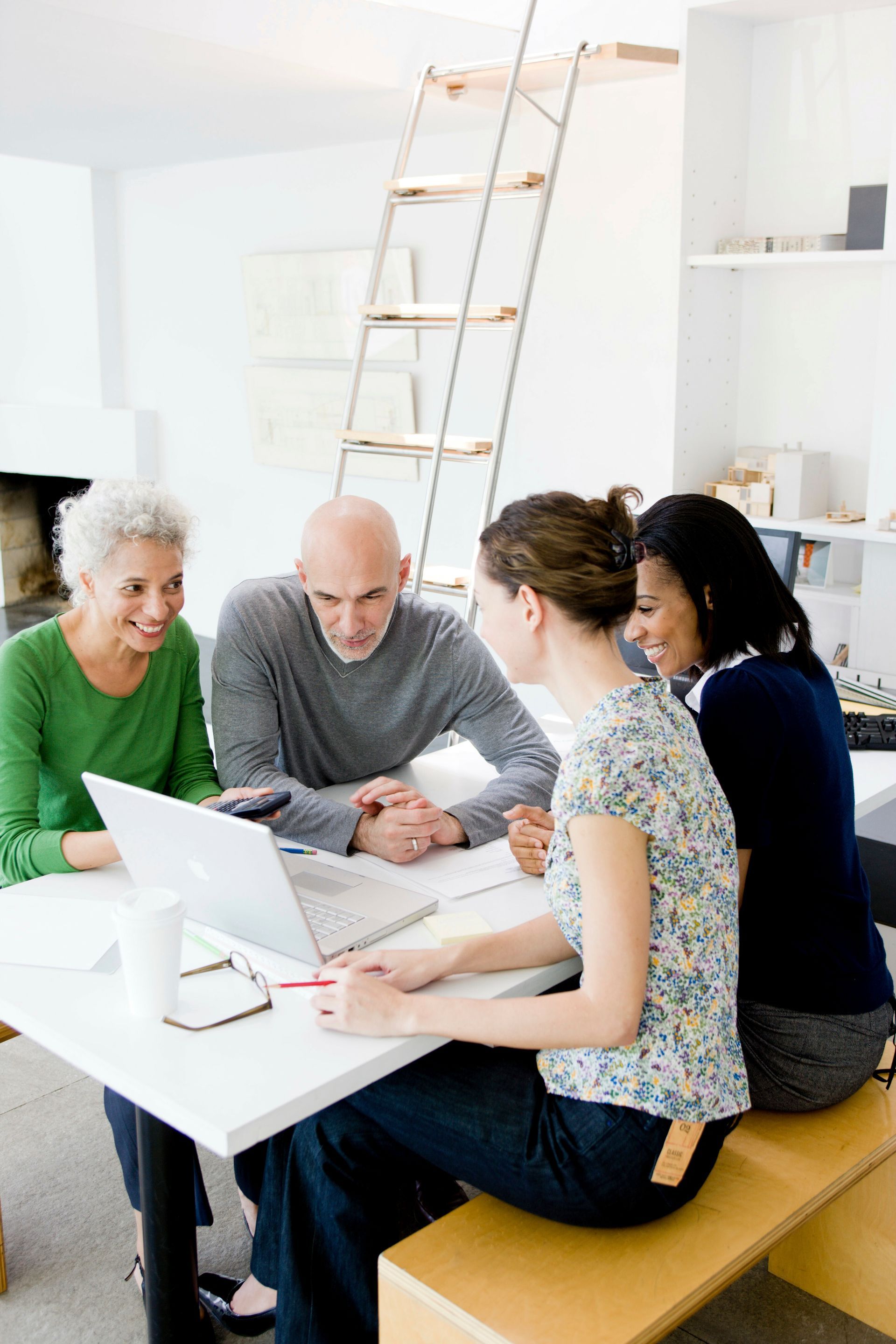 A group of people are sitting around a table looking at a laptop.