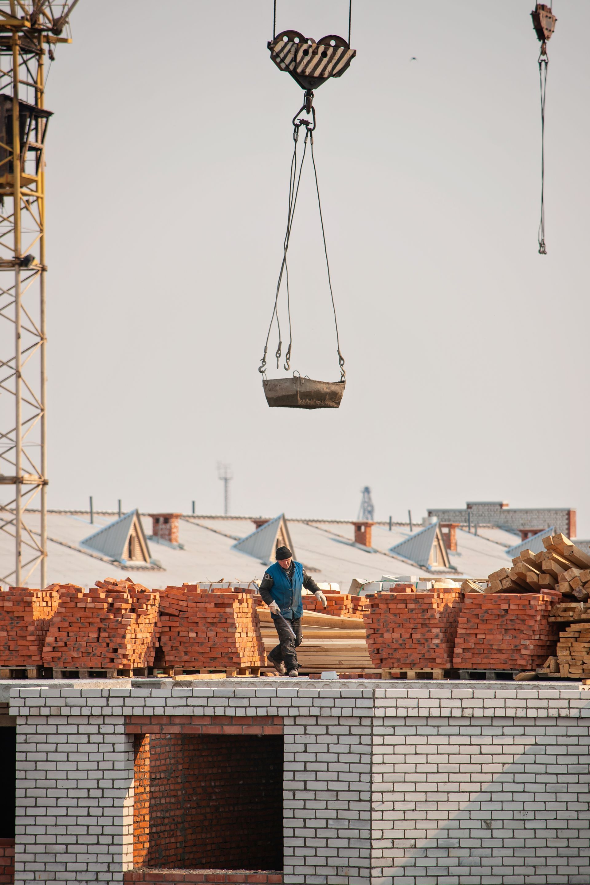 A man is standing on top of a brick building while a crane lifts a load of bricks