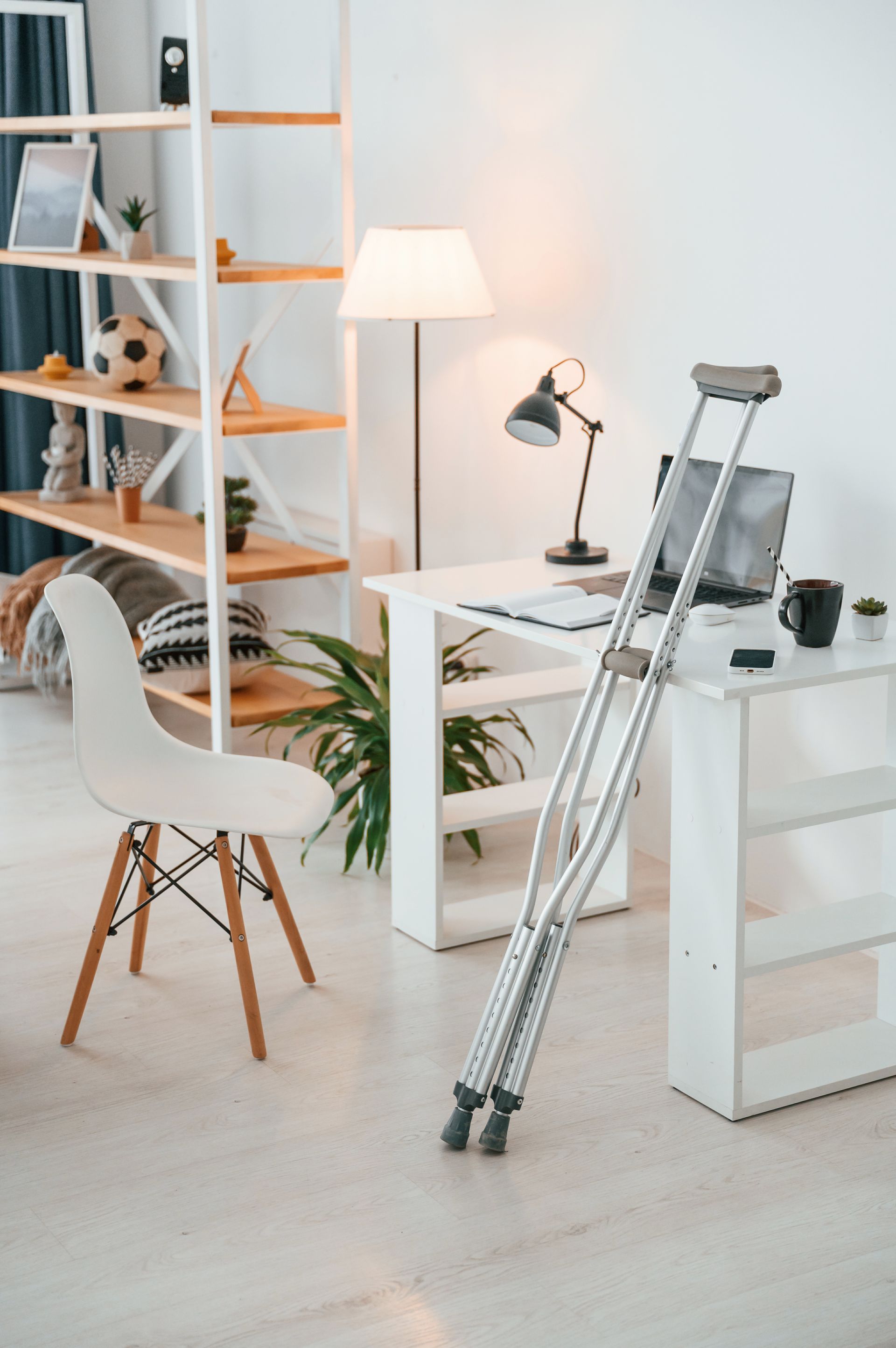 A person with crutches is sitting at a desk in a living room.