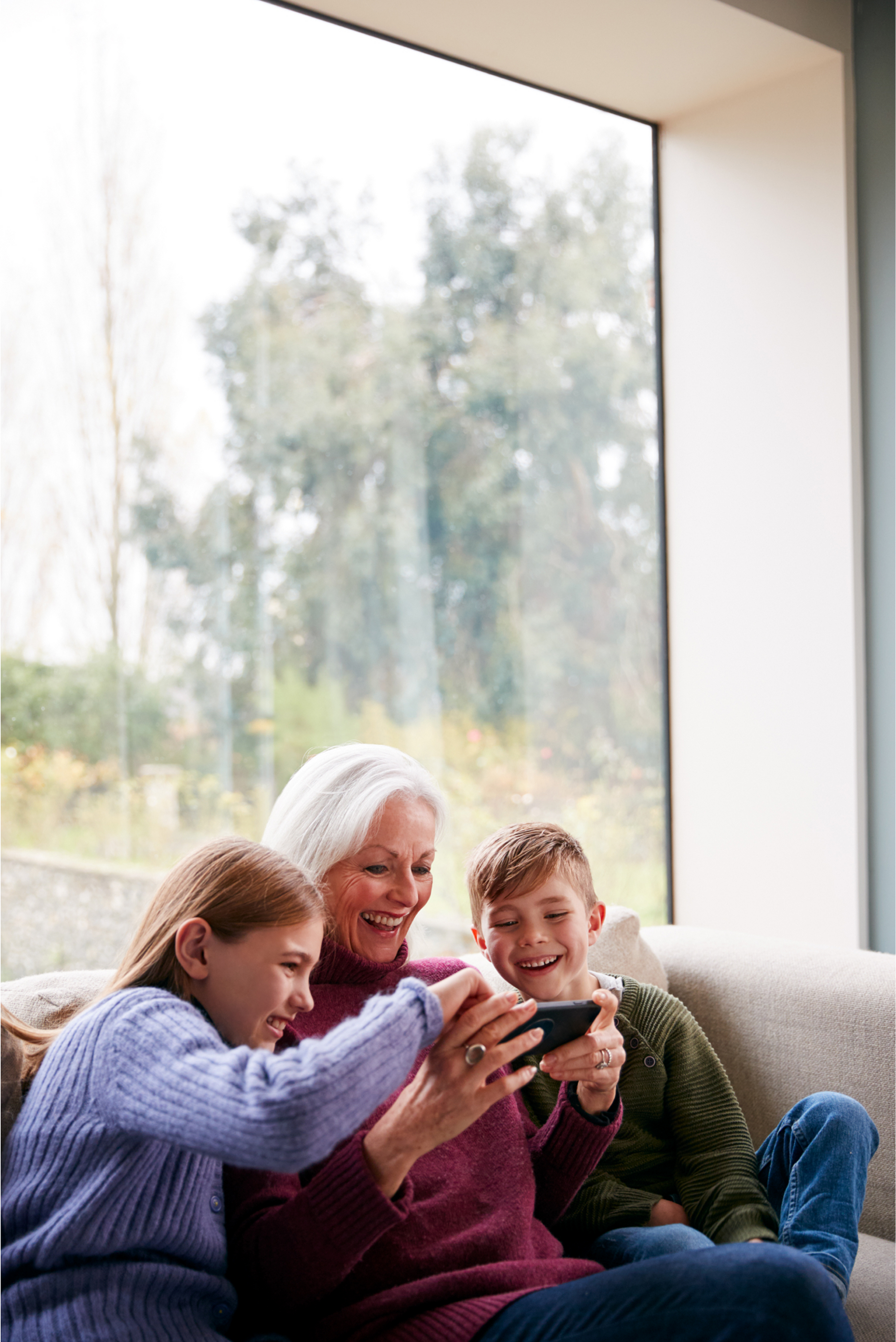 A woman and two children are sitting on a couch looking at a cell phone.