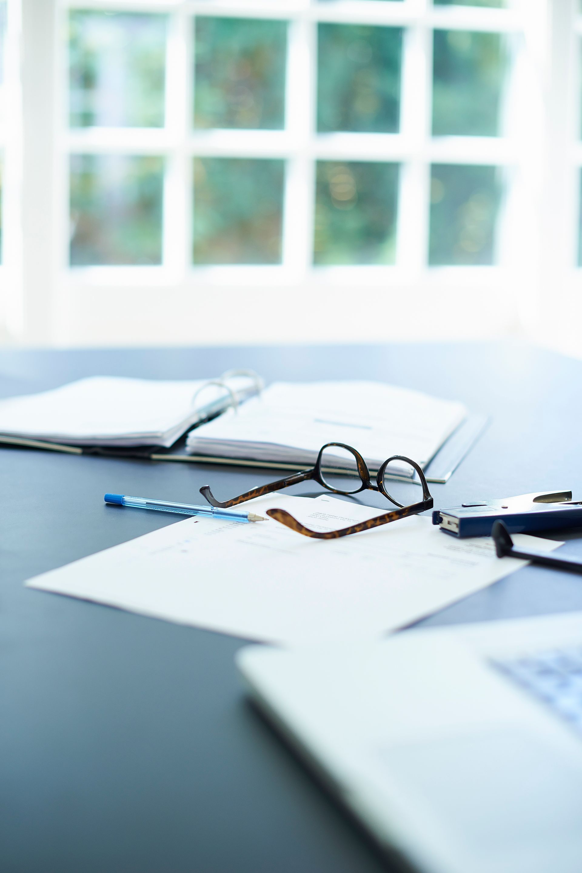 A desk with papers , glasses , a pen , and a laptop.