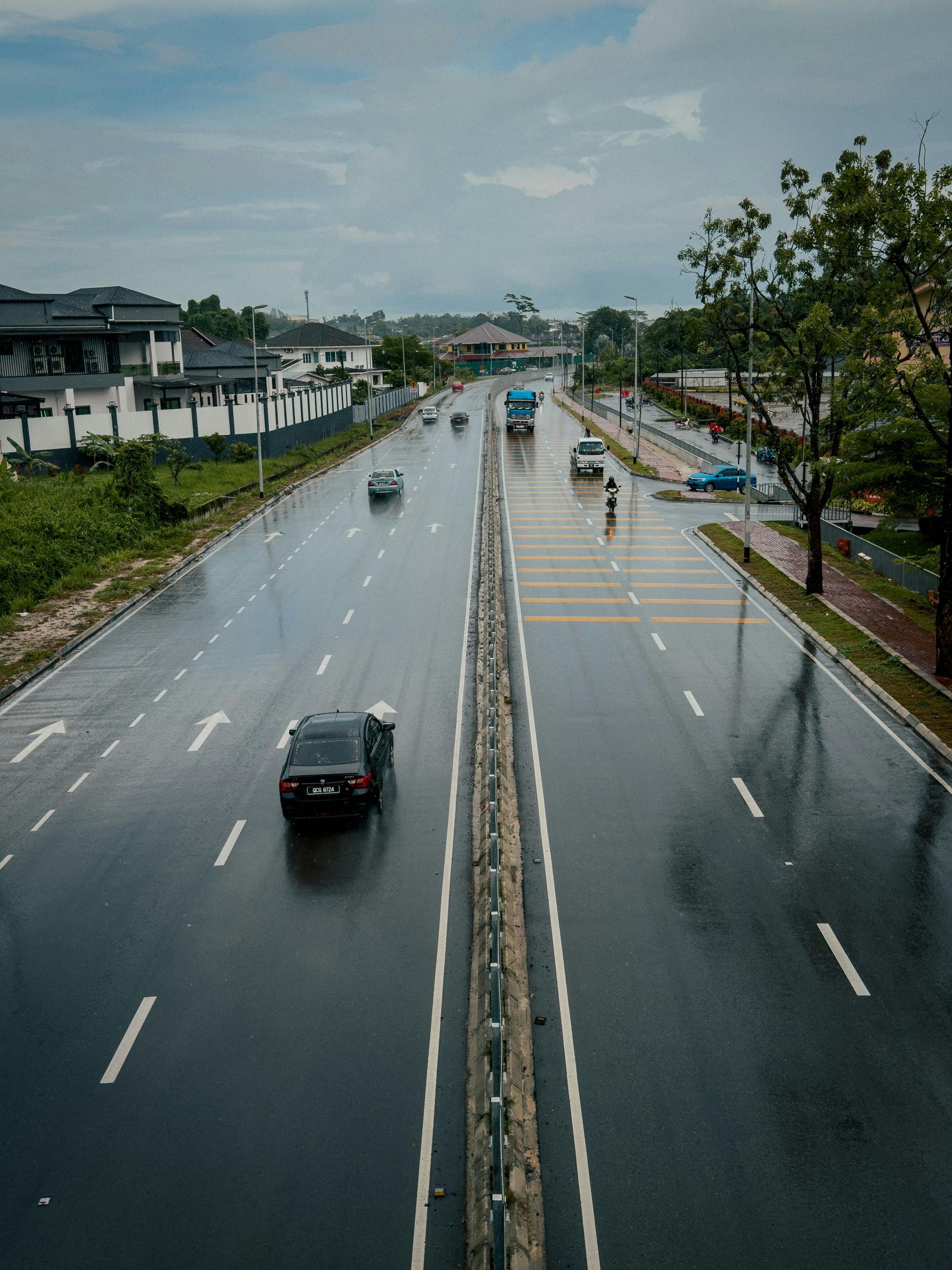 Wet highway with cars driving. Grey sky, trees, and buildings.