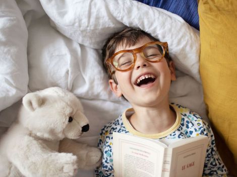 Un ragazzino con gli occhiali è sdraiato a letto e legge un libro.